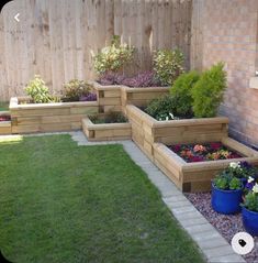 several wooden planters with flowers in them near a brick wall and green grass on the ground