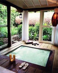 an indoor hot tub with candles and sandals on the floor in front of large windows