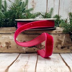 a red ribbon on top of a wooden box with pine branches in the back ground