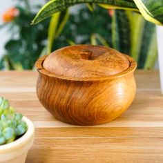 a wooden bowl sitting on top of a table next to a potted plant