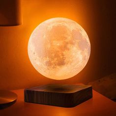 the moon lamp is lit up on a table next to a wooden block and lampshade