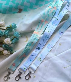 two blue lanyards with flowers and scissors on top of white fabric next to each other