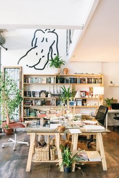 a room filled with lots of books and plants next to a wooden table topped with potted plants