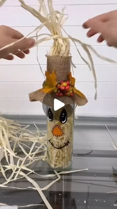 two hands reaching out towards a fake scarecrow in a jar with straw and leaves on it