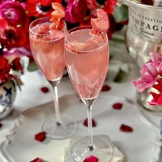 two champagne flutes with strawberries in them sitting on a tray next to red flowers