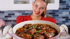 a woman in a red dress is holding a large bowl of food with meat on it