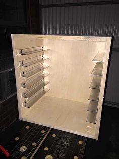 the inside of a white box with shelves and tools in it on top of a table