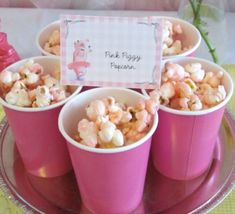 pink cups filled with marshmallows on top of a cake plate next to candy