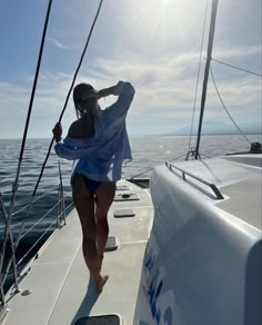 a woman standing on the bow of a sailboat in the ocean, with her back to the camera