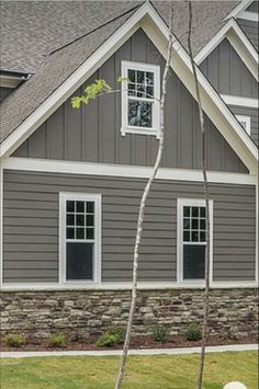 a gray house with white trim and windows on the front, along with two trees