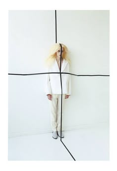 a woman with long blonde hair standing in front of a white wall and black lines