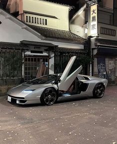 a silver sports car parked in front of a building with its doors open on the street