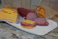 meat, cheese and crackers on a cutting board with plastic bags over them sitting on a marble counter top