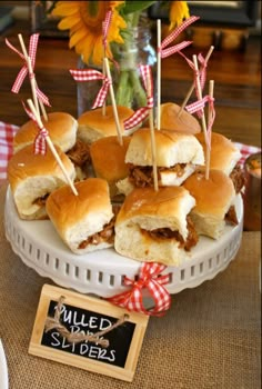 small sandwiches with toothpicks in them on a white plate next to sunflowers