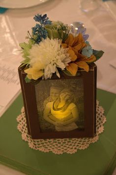 a small box with flowers on top of it and a lit candle in the middle