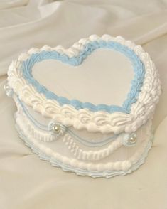 a white and blue heart shaped cake sitting on top of a tablecloth covered bed