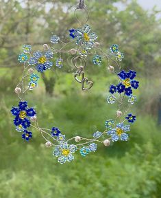 a blue and yellow flowered glass sun catcher hanging from a window with trees in the background