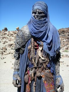 a person wearing a blue scarf and headdress standing in front of some rocks