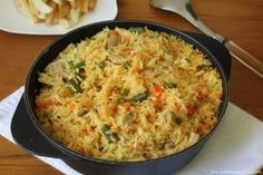 a pan filled with rice and vegetables on top of a table next to a plate of fries