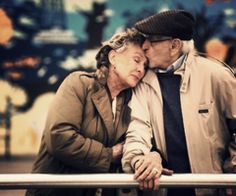 an older man and woman are kissing on a rail outside in the city at night