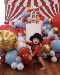 a little boy in a red shirt and black hat is posing for a photo surrounded by balloons