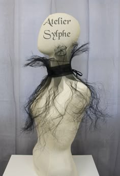 a white mannequin head with black hair and a sign on it that says atelier sylphe