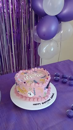 a pink birthday cake sitting on top of a table next to purple and white balloons