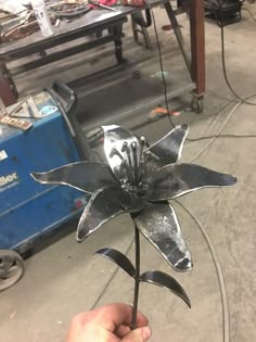 a person holding a metal flower in their hand with other tools behind them on the table