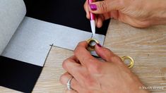 someone cutting out some paper with scissors on a wooden table next to a black and white striped wall