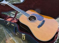 an acoustic guitar sits in its case on a bench