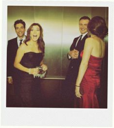 two men and a woman standing next to each other in front of a wall mounted mirror