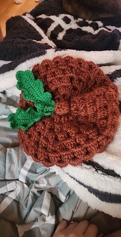 a crocheted hat with a green leaf on it laying on top of a bed