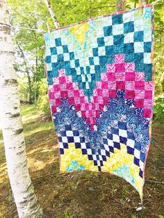 a colorful quilt hanging from a tree in the woods