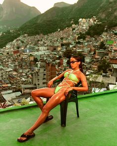 a woman sitting on top of a green chair in front of a cityscape