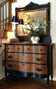 a wooden dresser sitting under a mirror next to a stair case with a vase on it