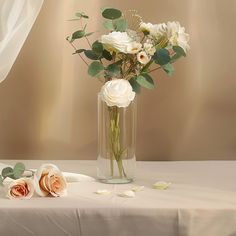 a vase filled with white flowers sitting on top of a table next to a curtain