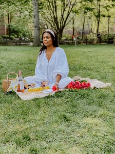 a woman sitting in the grass with food and drinks