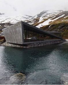 an instagramted photo of a house in the middle of water with snow covered mountains behind it