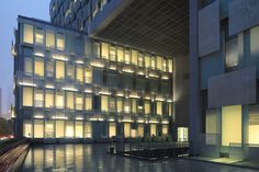 a building with lots of windows lit up in the dark at night, and water reflecting on the ground