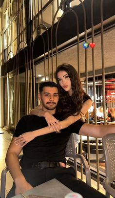 a man sitting next to a woman on top of a metal chair in front of a building