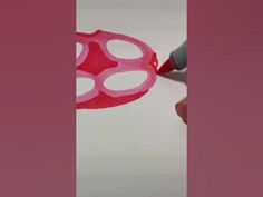 someone is drawing something on the paper with pink marker and red plastic ring around it