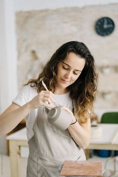 a woman is working on something in her home studio, while holding a cup and scissors