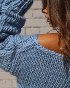 a woman with long hair wearing a blue knitted sweater and holding her arm behind her back