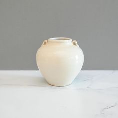 a white vase sitting on top of a marble counter next to a gray wall and floor