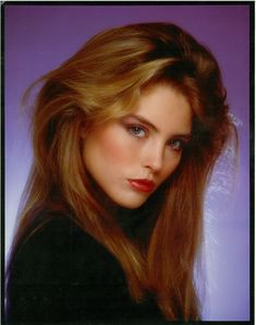 a woman with long brown hair posing for a photo in front of a purple background