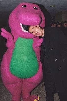 a man standing next to a large purple dinosaur mascot with his face close to the ground