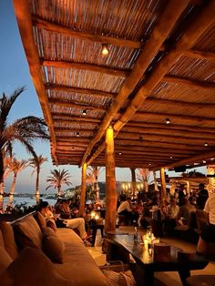 an outdoor seating area with palm trees and water in the background