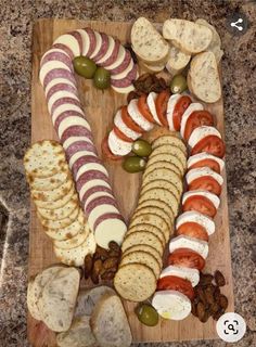 a wooden cutting board topped with different types of appetizers next to crackers and olives