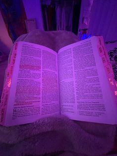 an open book sitting on top of a bed next to a purple light in a room