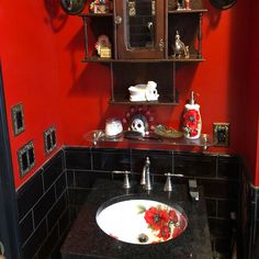 a bathroom with red walls and black counter tops, decorated with flowers on the sink